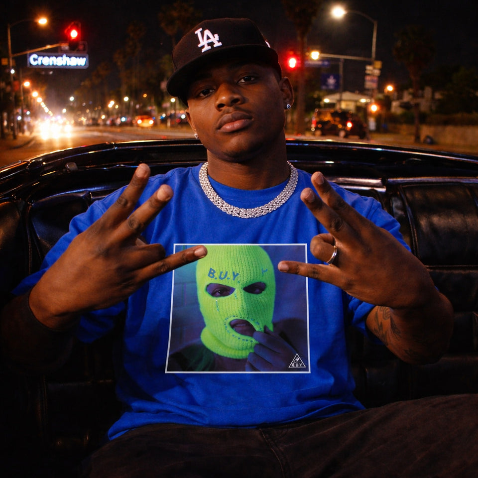 Person wearing a blue shirt with a graphic of a green mask and text, sitting in a car at night.