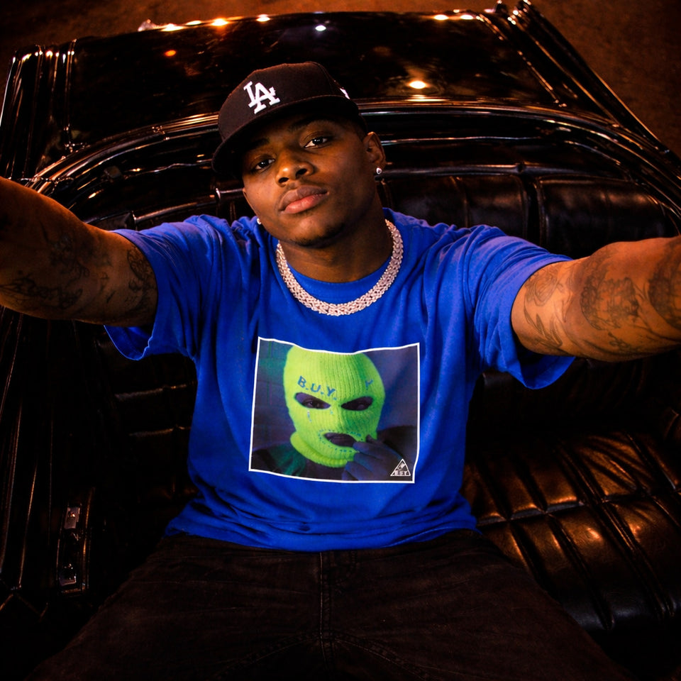 Person wearing a blue t-shirt with a graphic design, sitting inside a vehicle.